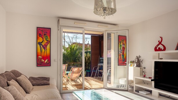 Una sala de estar con un sofá, una mesa de centro de vidrio, un televisor y un ventanal corredero que da a un patio exterior.
