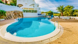Une piscine avec un bâtiment blanc en arrière-plan, entourée de verdure et sous un ciel dégagé.