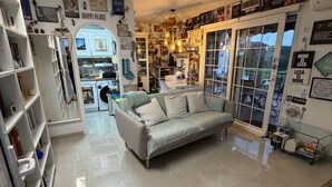 Un salon bien éclairé, avec un canapé, une table basse et une bibliothèque. Une porte donne sur un balcon.
