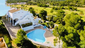 Un grand bâtiment blanc doté d’une piscine, entouré de verdure et de collines.