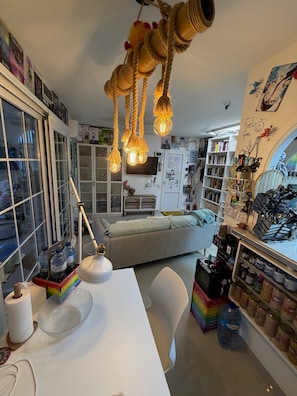 Un espace de vie chaleureux comprenant un canapé, une table avec une lampe, une bibliothèque et un coin cuisine équipé d’un four à micro-ondes.