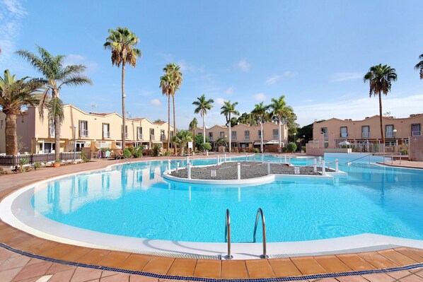 Une piscine de forme circulaire, entourée de palmiers et de bâtiments d  ’hôtel.