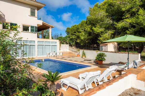 Una casa moderna de dos pisos con piscina, mobiliario exterior y jardín.