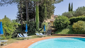 A swimming pool with lounge chairs and umbrellas, surrounded by greenery and a stone building. - Holiday Home 'La Ripa - Appartamento I Nidi' with Shared Pool, Garden & Wi-Fi (San Gimignano)