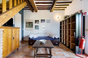 A living room with a wooden table, a sofa, a television, and a bookshelf. - Holiday Home 'La Ripa - Appartamento I Nidi' with Shared Pool, Garden & Wi-Fi (San Gimignano)