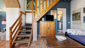 A staircase with wooden railings, a wooden cabinet, a television, a sofa, and a tiled floor. - Holiday Home 'La Ripa - Appartamento I Nidi' with Shared Pool, Garden & Wi-Fi (San Gimignano)