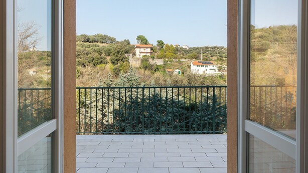 A balcony with a view of a hilly landscape, a green metal fence, and a tiled floor.