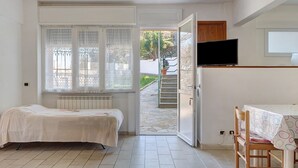 A bedroom with a bed, a TV, a dining table, and a view of a garden.