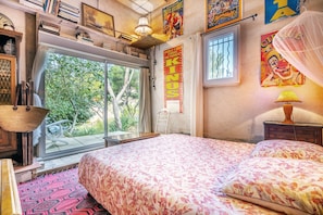 A bedroom with a large bed, a window, a ladder, and a poster on the wall.
