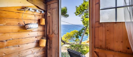 Interior de una cabaña de madera con vista al mar, un banco de madera y una cesta colgante.