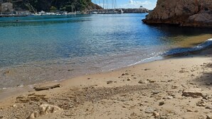 A beach with clear water, a rocky shoreline, and boats in the distance.