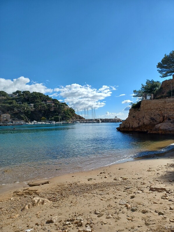 A beach with clear water, a rocky shoreline, and boats in the distance.