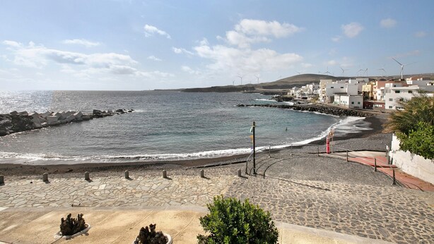 Une vue sur la côte, avec une promenade dallée, une plage et des éoliennes visibles au loin.