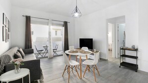 Un salon moderne avec un canapé gris, une table de salle à manger ronde entourée de chaises blanches, un meuble TV noir et un luminaire suspendu au plafond.