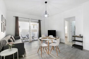Un salon moderne avec un canapé gris, une table de salle à manger ronde entourée de chaises blanches, un meuble TV noir et un luminaire suspendu au plafond.
