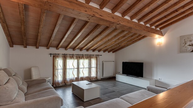 Un salon moderne avec un haut plafond en bois, un téléviseur à écran plat, un canapé, une table basse et une fenêtre avec des rideaux.