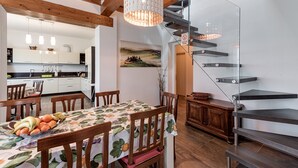 Un coin repas avec une table dressée pour quatre personnes, un escalier et une cuisine en arrière-plan.