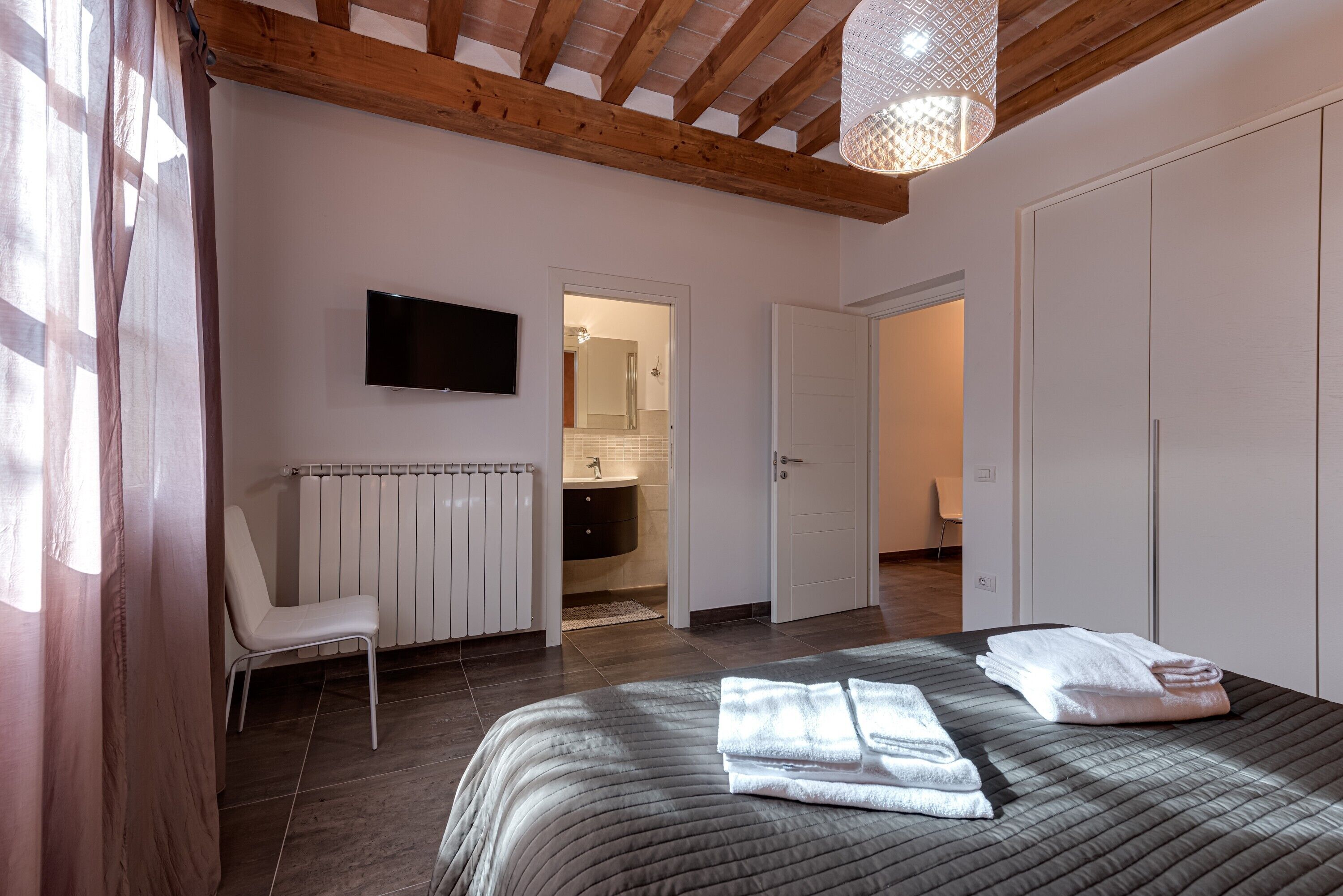 A bedroom with a bed, a chair, a television, a bathroom, and a wardrobe.