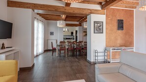 Un salon moderne avec un plafond en bois, un coin repas avec des chaises et une table, et une cuisine à l’arrière-plan.