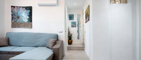 Ein modernes Wohnzimmer mit einem Ecksofa, einem floralen Dekorationsbild und einem Flur, der zu einer Tür führt.