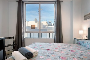 Una habitación de hotel con cama, una silla, un escritorio, una lámpara y una ventana con cortinas.