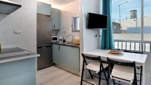 Una cocina compacta con microondas, cafetera y televisor montado en la pared.