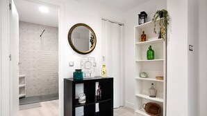 Un pasillo con una consola negra, un estante blanco con adornos y una puerta blanca.