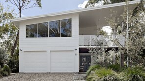 A modern two-story house with a white exterior, large garage doors, and a covered porch area. - Ocean At Bendalong - The Epitome of Coastal Elegance (Bendalong)