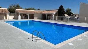 A rectangular swimming pool with clear blue water, surrounded by a tiled deck and covered seating areas. - Charming air-conditioned two-bedroom house with mezzanine, veranda, sleeps five, terrace, WiFi,... (PORTIRAGNES)