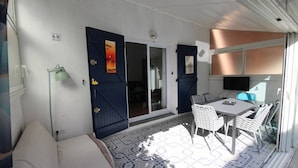 A sunlit patio with a dining table and chairs, a sofa, and a sliding glass door leading to an interior space. - Charming air-conditioned two-bedroom house with mezzanine, veranda, sleeps five, terrace, WiFi,... (PORTIRAGNES)