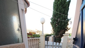 A tiled patio with a geometric pattern, a white gate, and a tall tree in the background. - Charming air-conditioned two-bedroom house with mezzanine, veranda, sleeps five, terrace, WiFi,... (PORTIRAGNES)