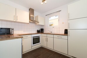 A compact kitchen with white cabinets, a microwave, an oven, and a coffee maker.