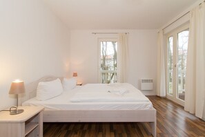 Un dormitorio moderno con una cama de madera, ropa de cama blanca, una lámpara de noche y una ventana con cortinas.