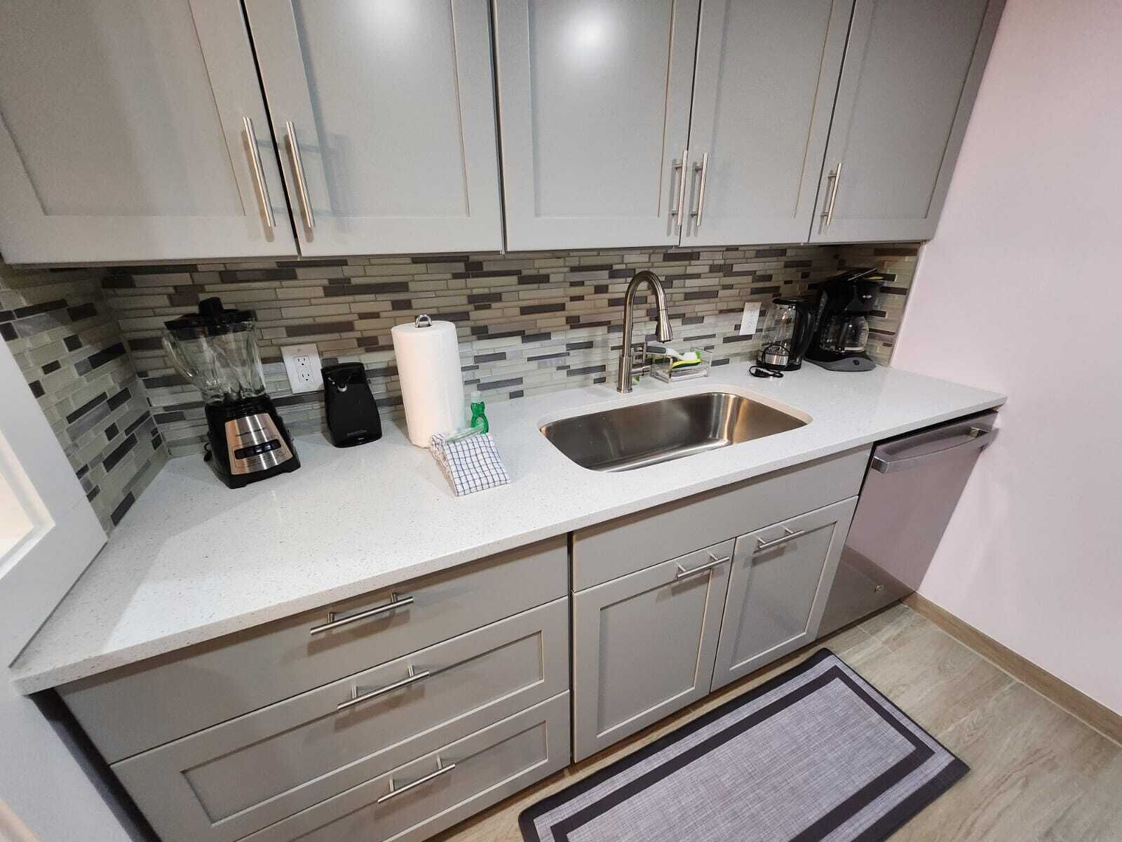 A kitchen with grey cabinets, a stainless steel sink, a coffee maker, and a blender on the counter.