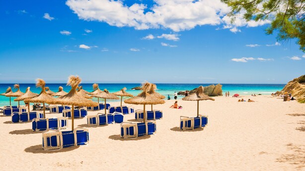 A beach with thatched umbrellas and blue lounge chairs. - Can Christin - central with pool (Cala Ratjada)