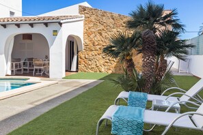 A poolside area with a stone wall, a covered seating area, and a palm tree. - Can Christin - central with pool (Cala Ratjada)