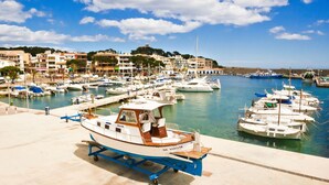 A marina with boats docked, a clear sky, and buildings in the background. - Can Christin - central with pool (Cala Ratjada)