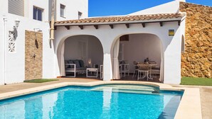 A swimming pool with a white exterior, stone wall, and a covered outdoor seating area with chairs and tables. - Can Christin - central with pool (Cala Ratjada)