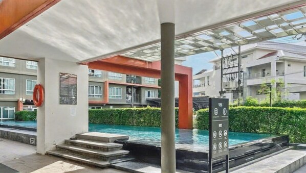 Zona de piscina exterior moderna con escalones de acceso, un flotador salvavidas y un cartel con símbolos.