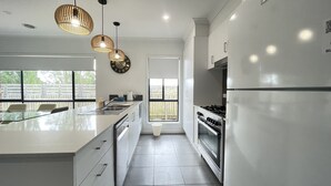 Een moderne keuken met een groot eiland, roestvrijstalen apparatuur en hangende lampen.