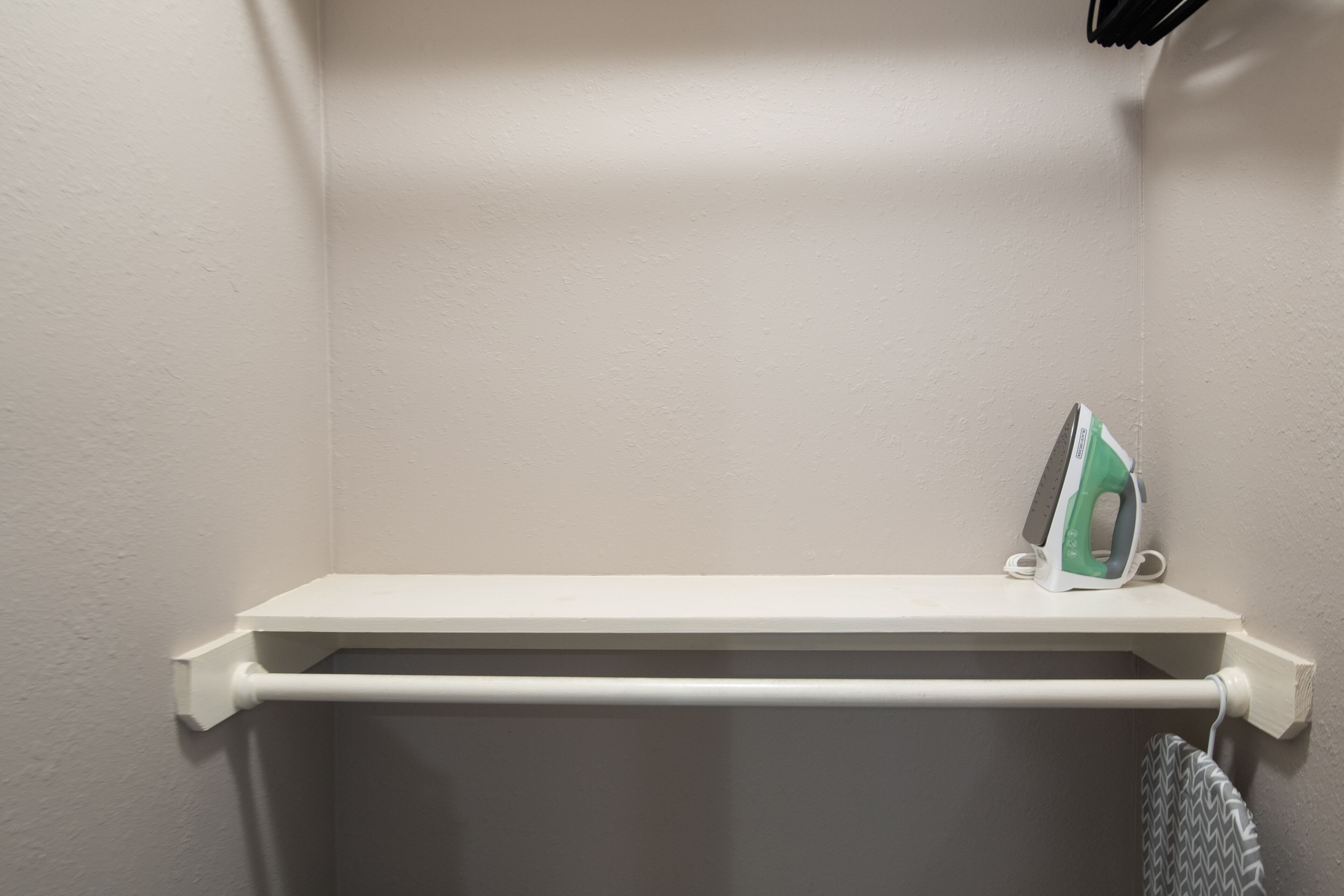 A white shelf with an iron and a towel hanging on a white wall.