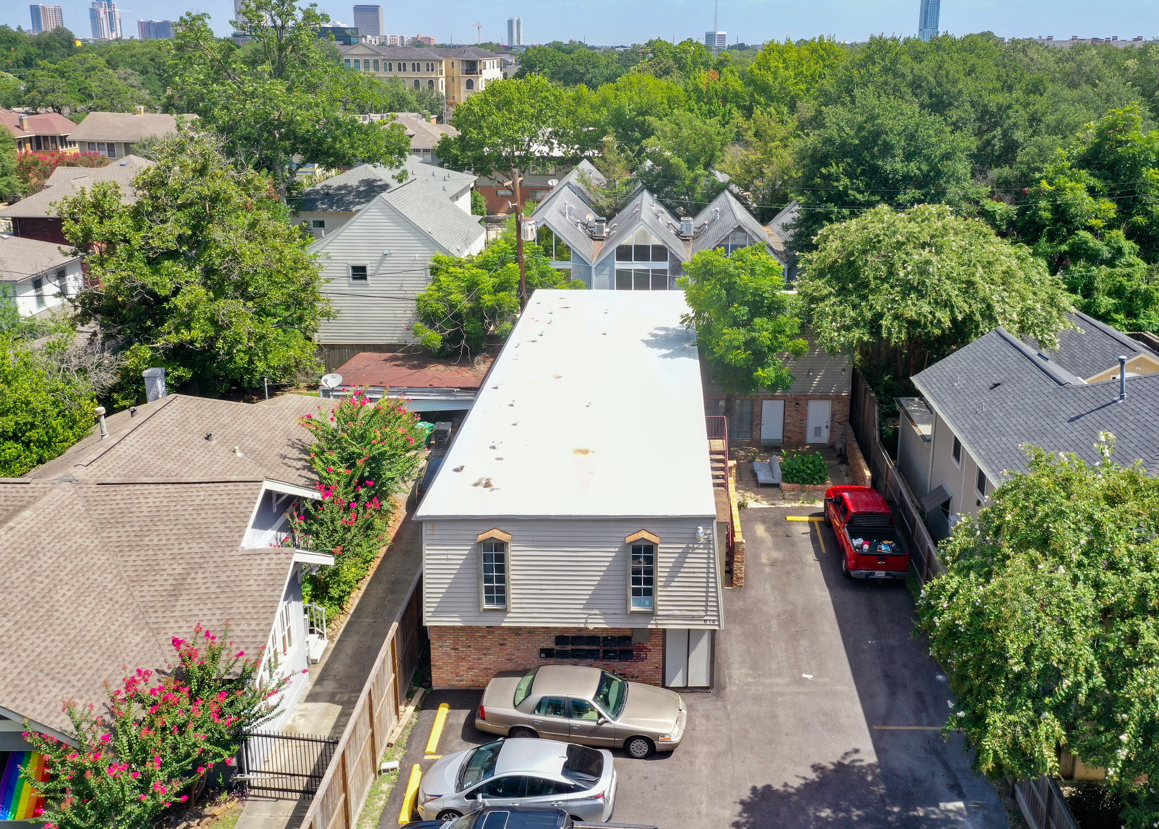 A residential building with a flat roof, a garage, and a parking area with cars.