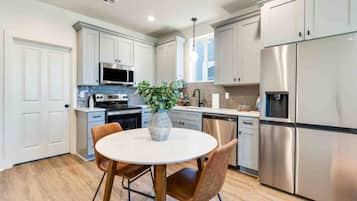 A modern kitchen with stainless steel appliances, white cabinetry, and a round dining table with chairs.