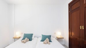 A hotel room with two beds, each with a teal pillow and a rolled towel. There are bedside lamps on wooden nightstands.