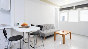A modern kitchen with white cabinets, a round dining table with black chairs, a grey sofa, and a small wooden table with a cup.