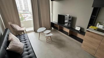 Un salon moderne avec un canapé, un téléviseur, une petite table et un fauteuil.