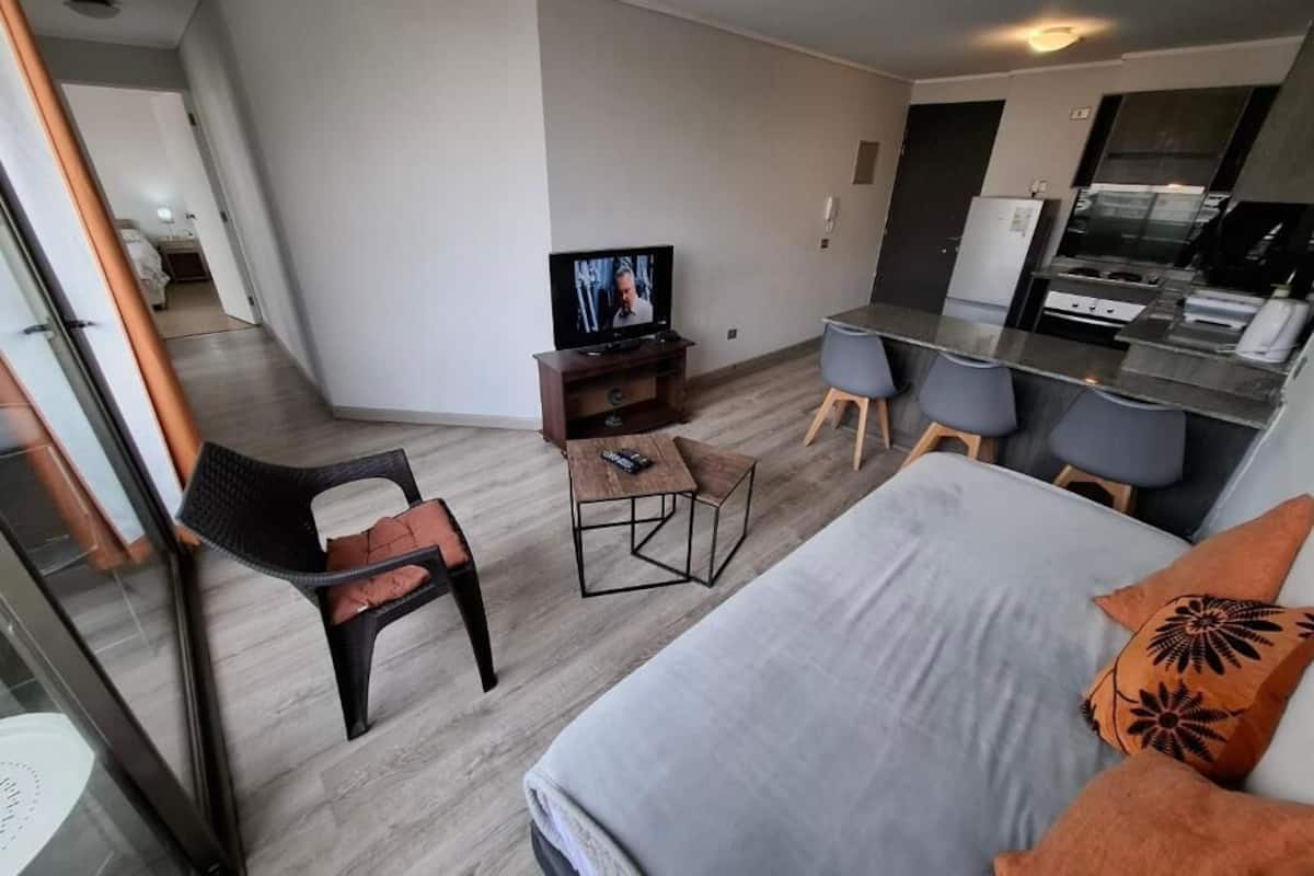 A modern hotel room with a bed, a TV, a small table, and a kitchenette.