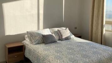 Un dormitorio con cama, mesitas de noche, una alfombra azul y una ventana con cortinas.