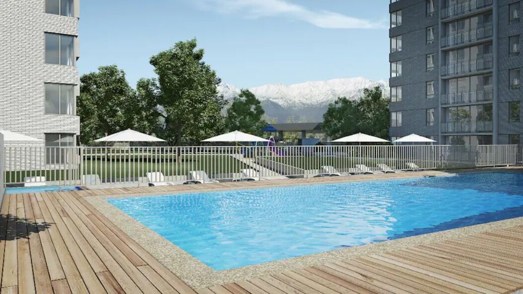 Una piscina con cubierta de madera, sillas de descanso, sombrillas y vista a las montañas.