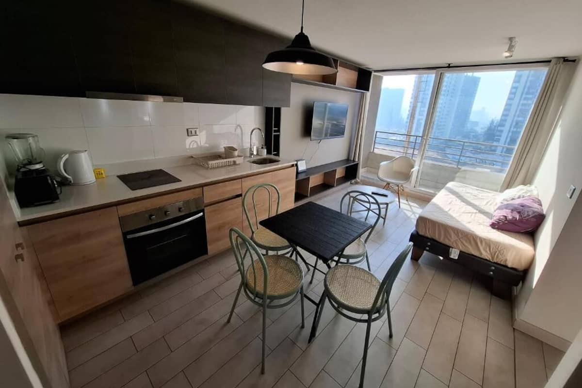 A modern kitchen with a dining area, a small balcony, and a bed.